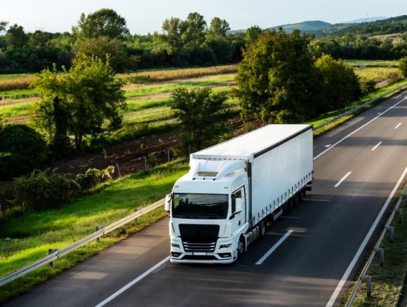 White truck driving on the highway winding through forested land