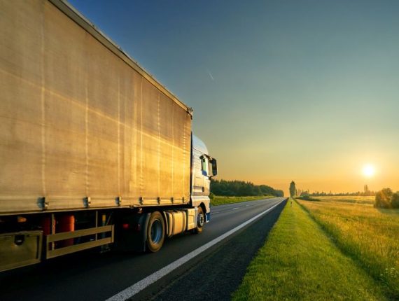 Truck driving on the asphalt road in a rural landscape in the golden sunset