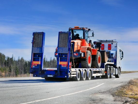 Semi trailer truck transporting wheel loader on highway on a beautiful day of spring, rear view.